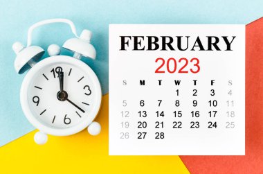 Renkli arkaplanda alarm saatiyle birlikte Şubat 2023 Aylık takvim yılı.