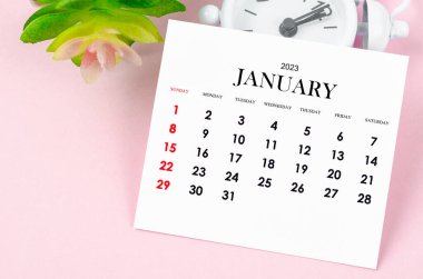 2023 yılının Ocak ayının takvimi. Pembe arka planda klasik çalar saat..