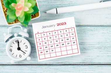 Ocak 2023 Aylık takvim yılı ve alarm saati mavi ahşap arka planda kalemle.