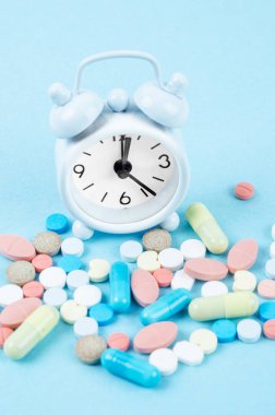 Beyaz alarm saati ve mavi arka planda bir sürü uyuşturucu. İlaçları doğru zamanda almak..