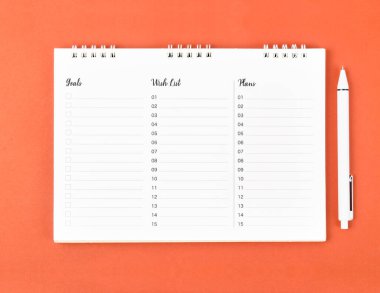 Planlama ve metni kaydetmek için turuncu arkaplan üzerine boş bir spiral defter ve beyaz kalem.