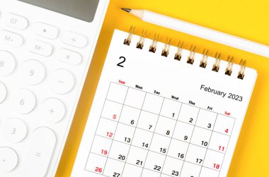 2023 yılı Şubat ayının masa takvimi ve sarı arka planda bir kalemle hesap makinesi..