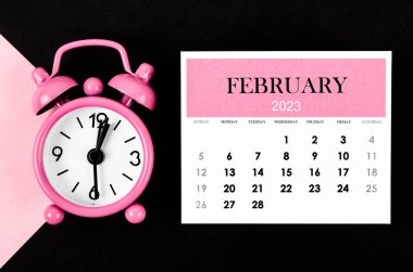 Pembe ve siyah arkaplanlı alarmlı takvim yılıyla Şubat 2023.