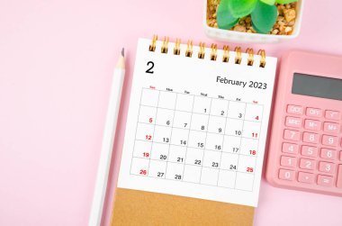 February 2023 desk calendar for 2023 year with calculator on pink color background.