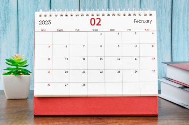 February 2023 Monthly desk calendar for 2023 year with the books on blue wooden background.
