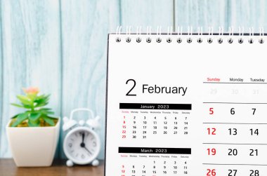 February 2023 Monthly desk calendar for 2023 year with alarm clock on blue wooden background.
