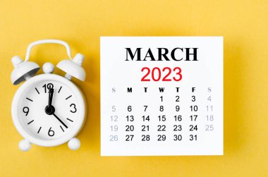 2023 Mart takvimine göre alarm saati sarı arka planda..