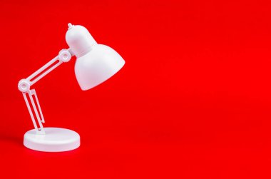 Kırmızı arkaplanda beyaz katlanır masa lambası.