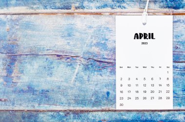 April 2023 calendar page hanged with white rope  on old blue wooden background.