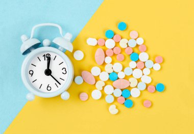 Beyaz alarm saati ve sarı arka planda bir sürü uyuşturucu. İlaçları doğru zamanda almak..