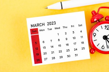 2023 Mart takvimine göre alarm saati sarı arka planda..