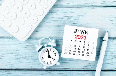 Aylık Haziran 2023 takvim yılı ve alarm saati mavi ahşap arka planda hesap makinesi ile.