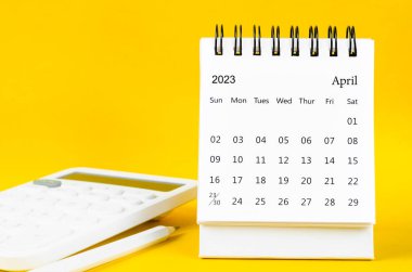 Nisan 2023 2023 Aylık masa takvimi ve sarı arka planda kalemle hesap makinesi.
