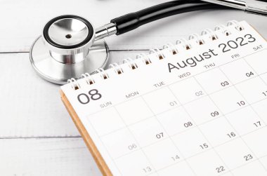 Stetoskop tıbbi ve Ağustos 2023 masa takvimi ahşap arka planda, sağlıklı kavramları kontrol etmek için takvim.