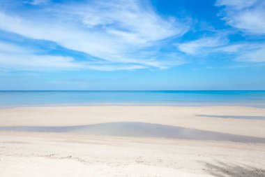 Güneşli sahil ve turkuaz deniz, berrak gökyüzü arka planı.