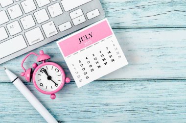 Temmuz 2023 Aylık takvim yılı ve alarm saati. Ahşap arka planda klavye bilgisayarı var..