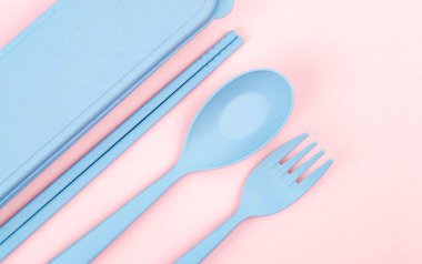 Pembe arka planda plastik kaşıklar, çatallar ve yemek çubukları seti.