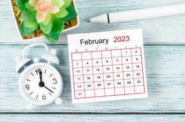 Aralık 2023 Aylık takvim yılı ve alarm saati mavi ahşap arka planda kalemle.