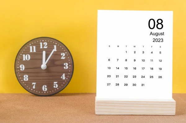 stock image August 2023 Monthly calendar for 2023 year  with clock on yellow table.