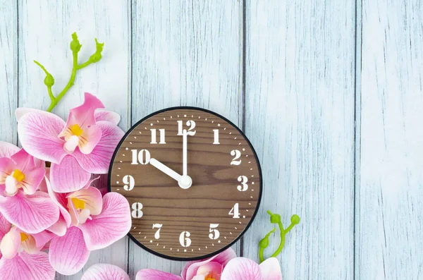 青い木製の背景に目覚まし時計とピンクの縞模様の蘭の花 — ストック写真