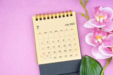 Temmuz 2023 takvim masası ve pembe arkaplanda pembe orkide.