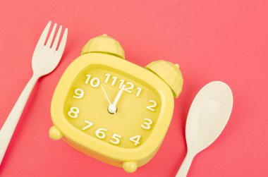 Kırmızı arka planda çatal bıçak takımı olan sarı alarm saati. Perhiz, öğle yemeği, diyet ve kilo kaybı kavramı