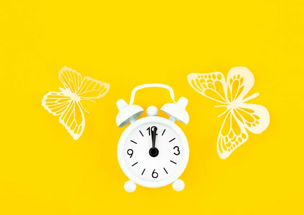 黄色の背景に白い目覚まし時計と紙の蝶 — ストック写真