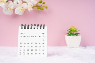 Temmuz 2023 masa takvimi ve beyaz orkide bir pembe arkaplan.