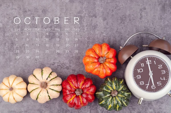 stock image October 2023 Calendar and pumpkins with alarm clock on black wood background.