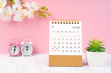 Temmuz 2023 alarm saati ve mermer zemin üzerinde beyaz orkide bulunan masa takvimi.
