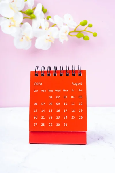 Red calendar August 2023. Desk calendar for year 2023 and pink orchid on pink background.