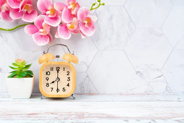 木製の目覚まし時計とあなたのデザインのためのコピースペースと木製の床にピンク色の蘭 — ストック写真