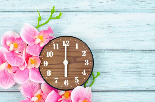 木製の目覚まし時計とピンクの縞模様の蘭の花青い木製の背景 — ストック写真