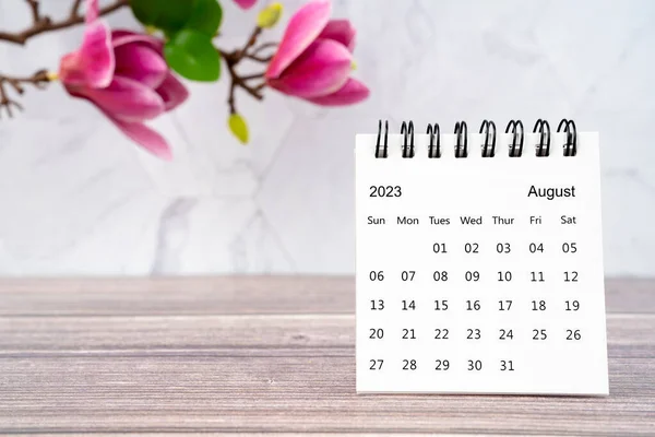2023年8月桌上日历和木制背景的白色粉红木兰花 — 图库照片