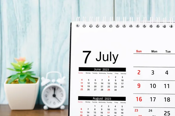 Stock image July 2023 Monthly desk calendar for 2023 year with alarm clock on blue wooden background.