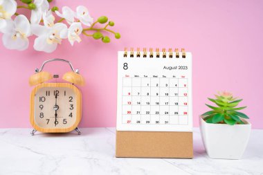 Tahta alarm saati ve mermer zeminde beyaz orkidesi olan 2023 Ağustosu masa takvimi.