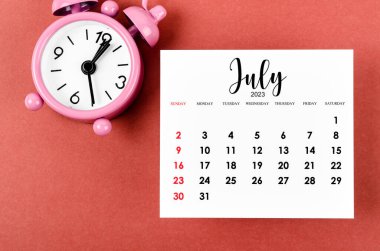 Kırmızı zemin üzerindeki alarm saatiyle birlikte Temmuz 2023 aylık takvim yılı.