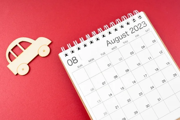 August 2023 desk calendar and wooden toy cars on red background.