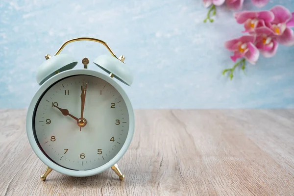 Vintage alarm clock on wood floor and pink color orchid decorate, empty room for background.