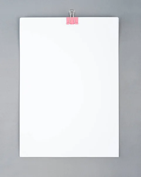 Pink color binder clip and blank white paper on gray color background for your text or message.