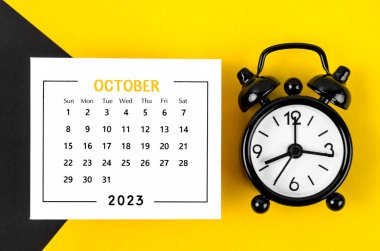 2023 yılının Ekim ayının takvimi. Arka planda siyah alarm saati var..