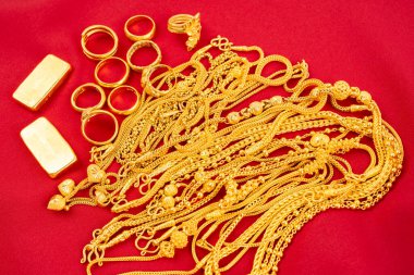 Kırmızı kadife arka planda birçok altın kolye ve altın külçeler.