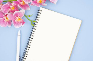 Metnin veya mesajın için pembe renk orkidesi olan boş bir defter ve kalem aç.