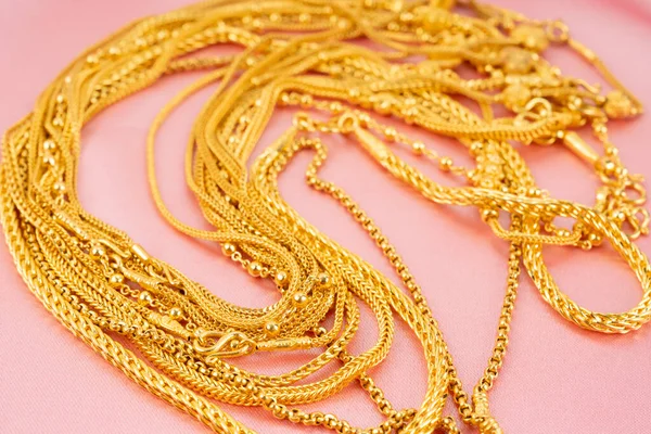 Много Золотых Ожерелий Фоне Розового Цвета Ткани — стоковое фото