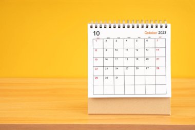Ekim 2023, 2023 tarihli aylık masa takvimi sarı arka planlı ahşap masada..