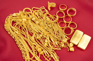 Kırmızı kadife arka planda bir sürü altın kolye ve altın külçeler..