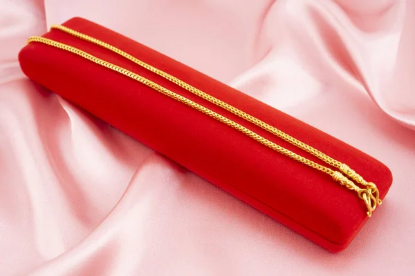 Gold necklace on a red velvet box on a pink fabric background.