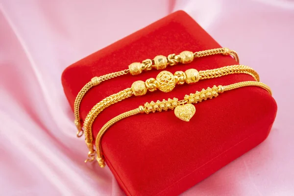 Many gold bracelet and red velvet box on the red silk background display.
