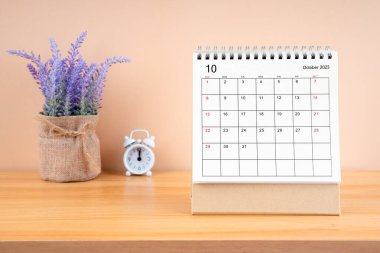 2023 yılının Ekim ayının masa takvimi ve ahşap masanın üzerindeki çalar saat..