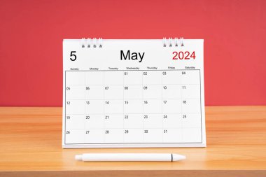 2024 yılı için aylık masa takvimi ve kırmızı arkaplan ile ahşap masa üzerinde kalem.